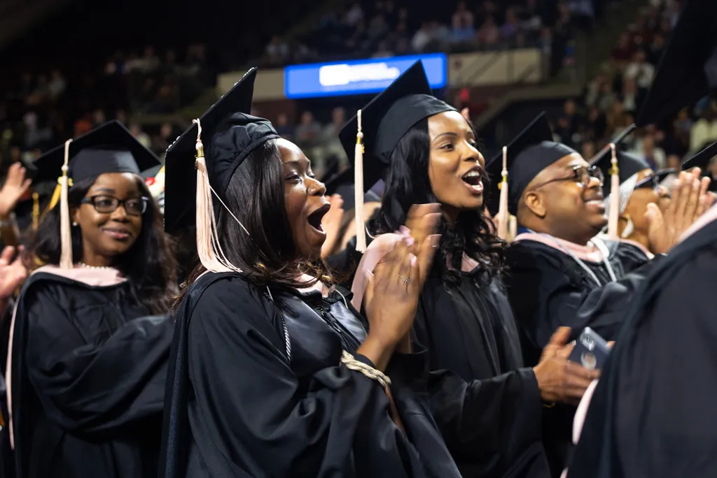 a group of U N E student wearing graduation regalia stand and applaud